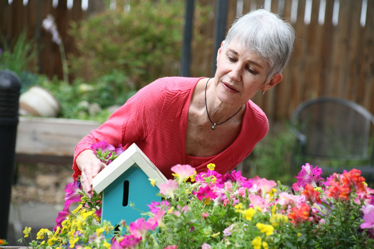 A woman tending to a colorful garden with a small birdhouse.