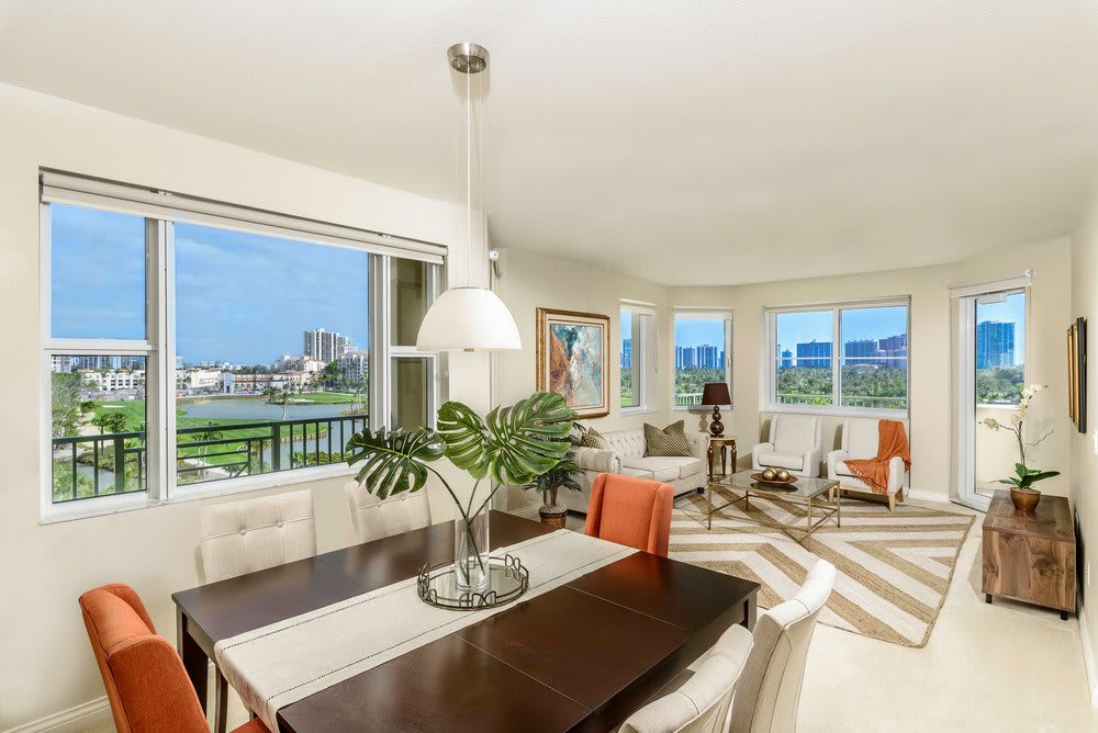 A modern living and dining area with large windows offering a city view, filled with natural light and decorated in neutral tones.