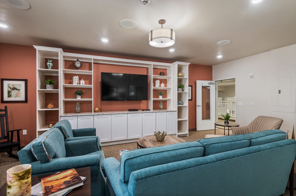 A modern living room with blue sofas, wall-mounted television, and built-in shelving units.