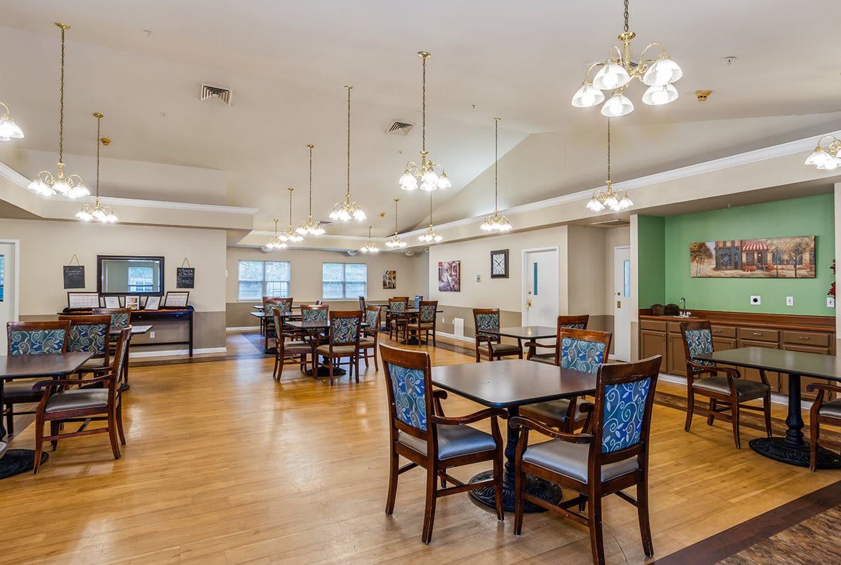 A spacious dining area with wooden floors, tables, and chairs under elegant lighting.