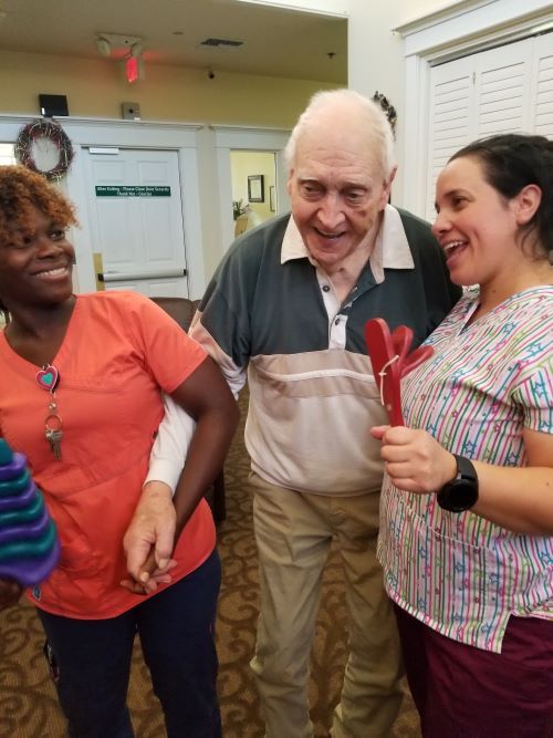 An elderly man smiles while standing with two caregivers in an indoor setting.