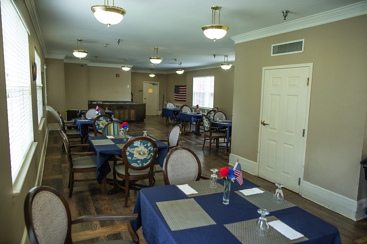 A well-arranged dining room with tables covered in blue tablecloths, decorated with small floral centerpieces.