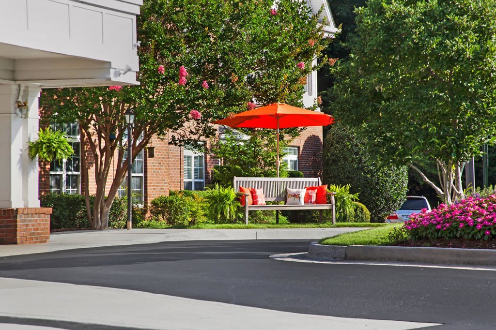 A serene outdoor seating area with a bench and red umbrella surrounded by lush greenery.