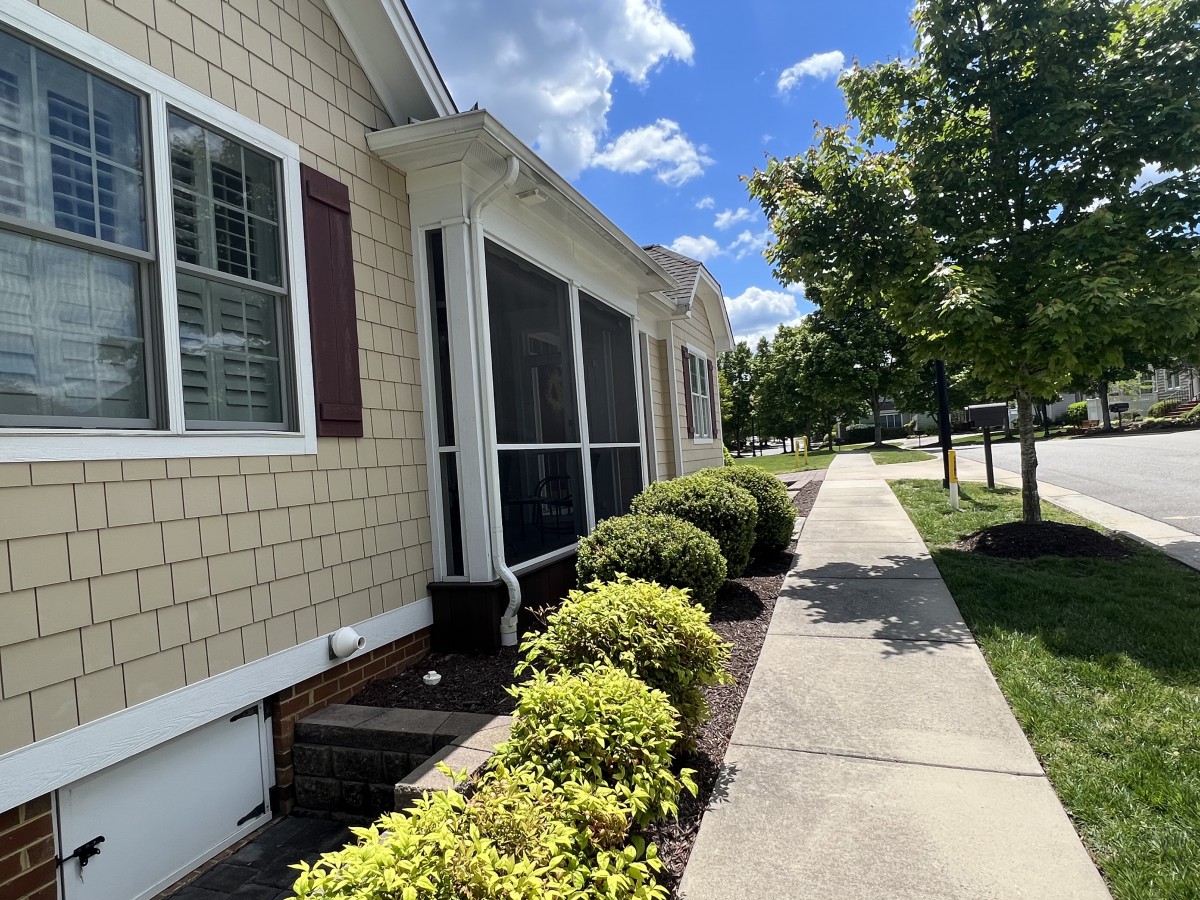 A sunny day view of a house with a sidewalk lined with bushes and trees.