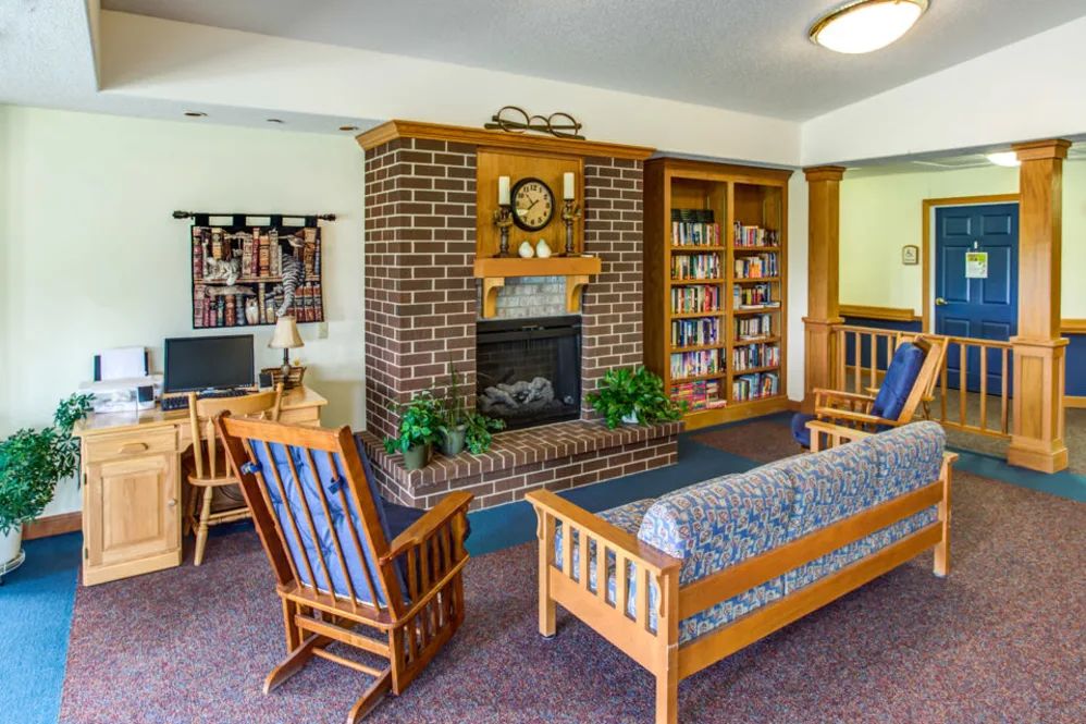 A cozy living room with a brick fireplace, wooden furniture, and a bookshelf.