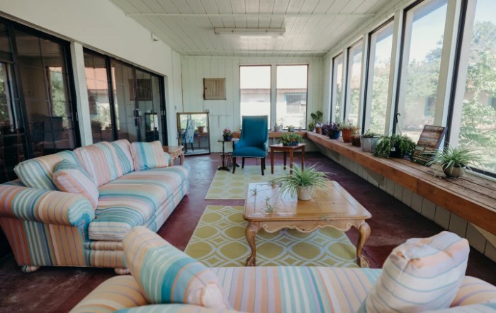 A cozy sunroom featuring striped sofas, a coffee table, and plenty of natural light.