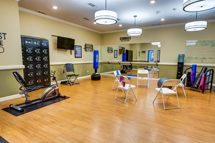 A spacious exercise room equipped with fitness machines, chairs, mirrors, and a television.