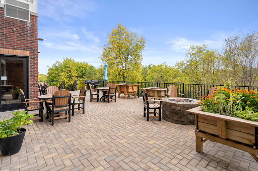 A serene outdoor patio area featuring comfortable seating and a fire pit, surrounded by lush greenery and clear blue skies.