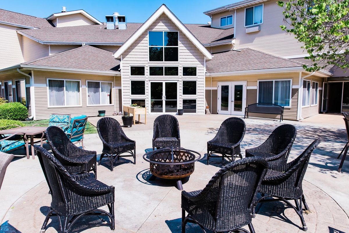 An outdoor patio area with wicker chairs arranged around a fire pit in front of a residential building.