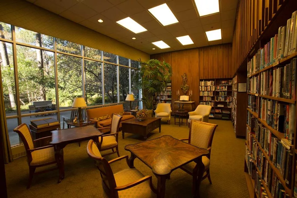 A cozy library reading room with wooden furniture and large windows letting in natural light.