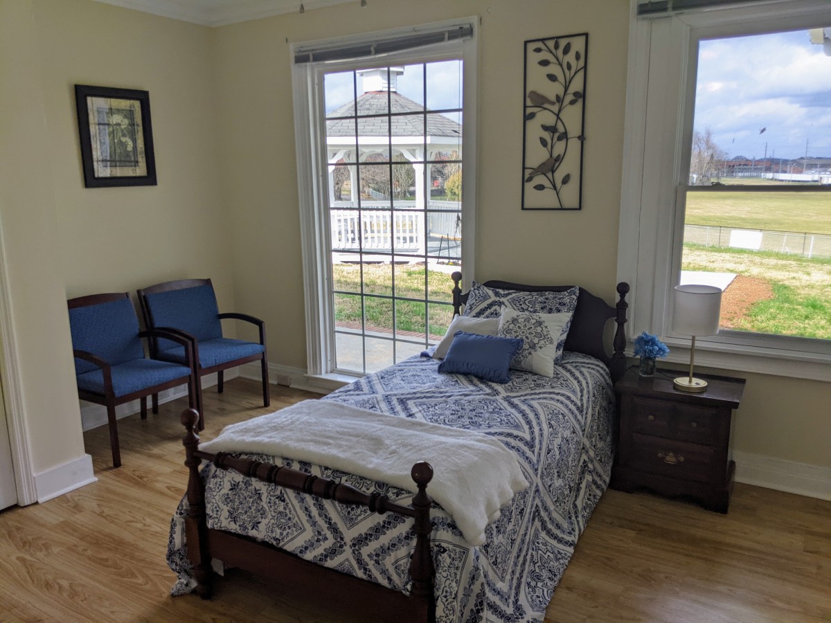 A cozy bedroom featuring a single bed with patterned bedding, two chairs, and large windows providing ample natural light.
