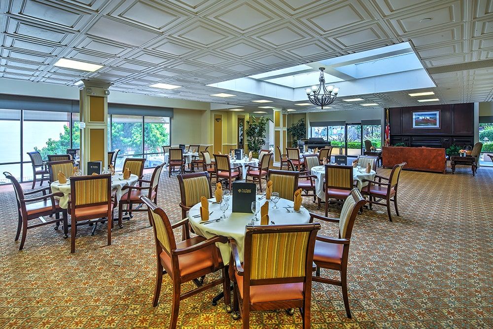 An elegant dining room with neatly arranged tables and chairs, featuring a skylight and chandelier.