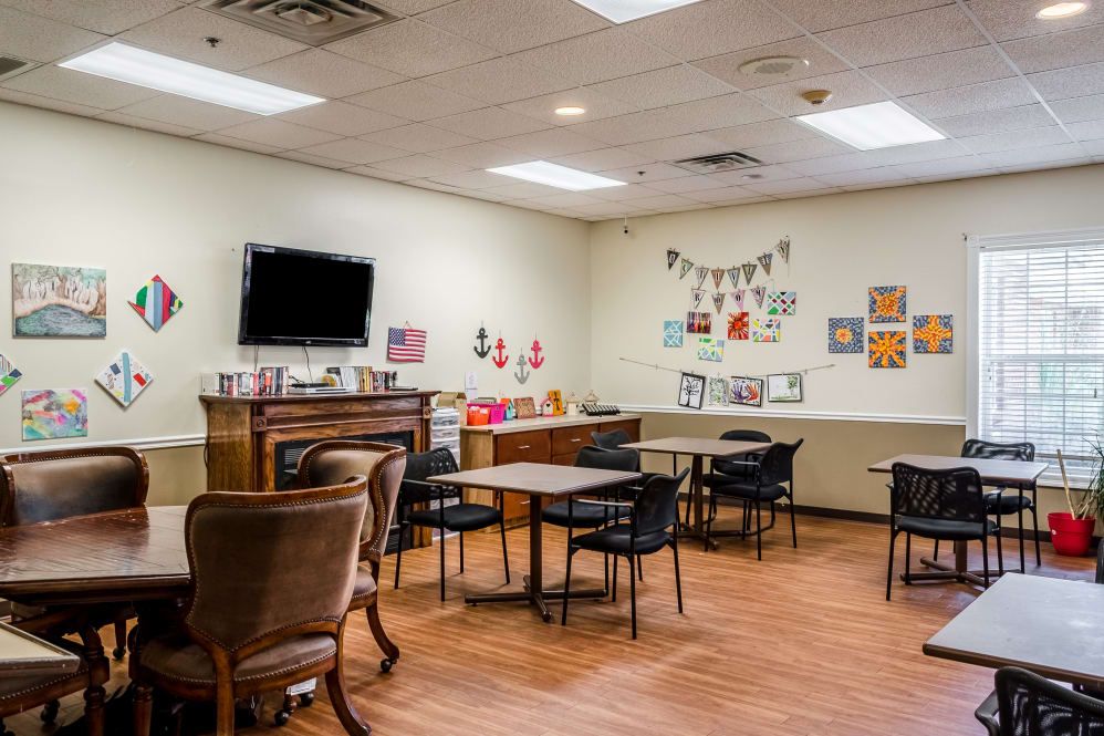 A cozy room with tables and chairs, decorated with artwork and a television mounted on the wall.