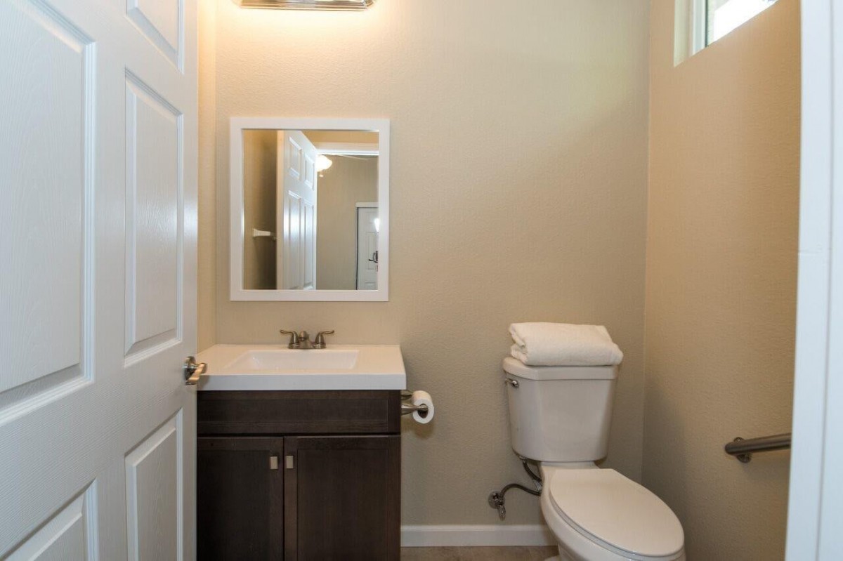A small, neatly arranged bathroom with a sink, mirror, toilet, and a light fixture.