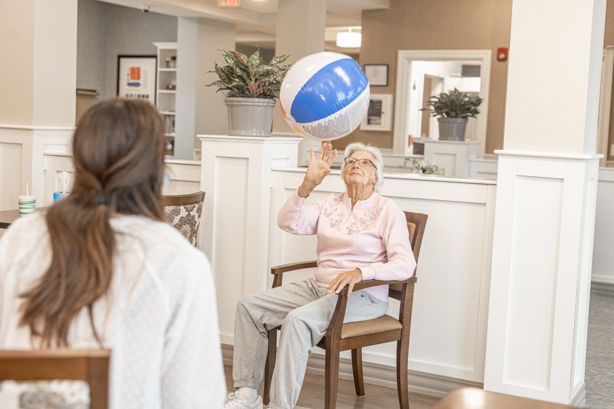An elderly woman playing with a beach ball indoors.