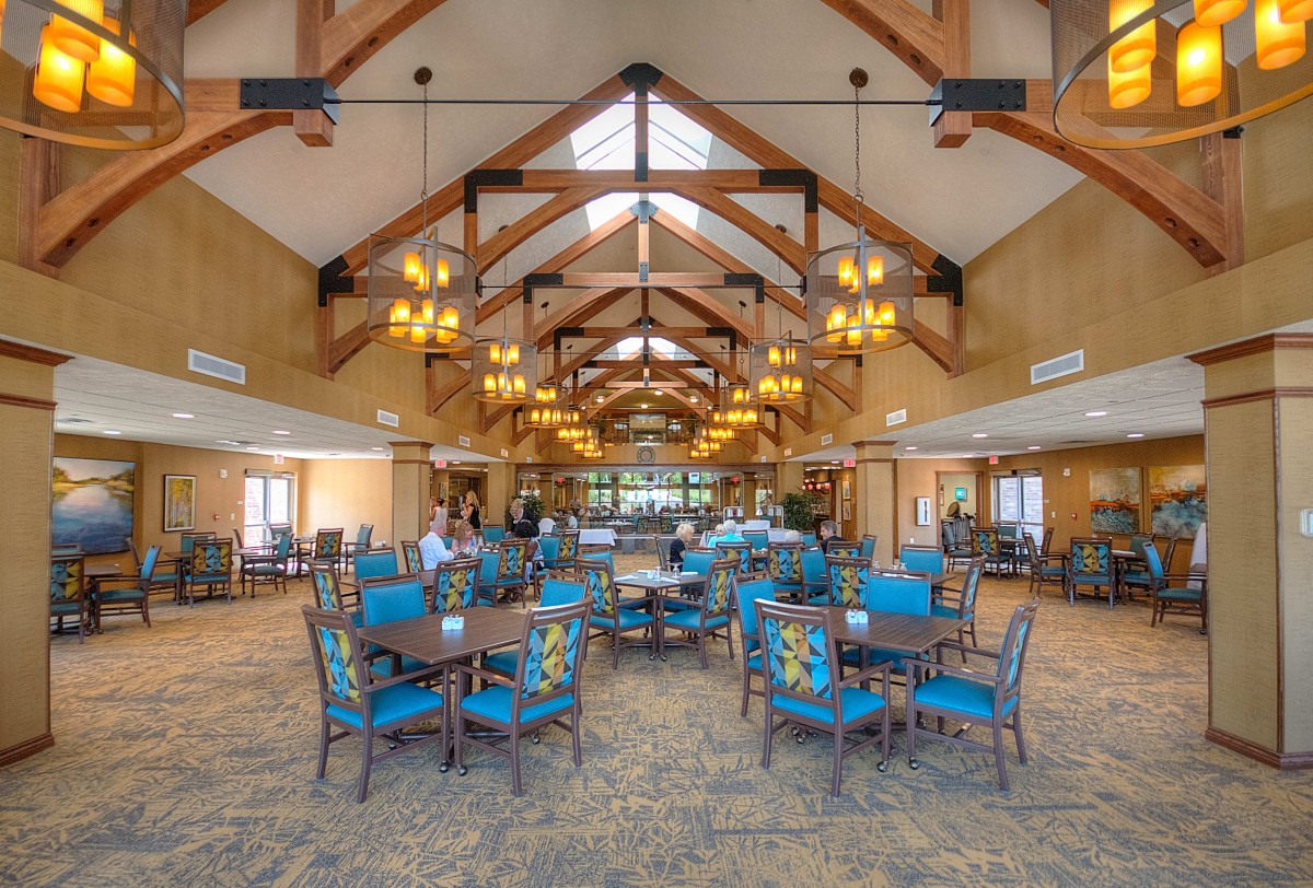 Spacious dining hall with wooden beams, blue chairs, and elegant chandeliers.