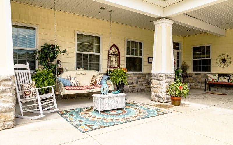 A cozy porch with a swing, plants, and decorative elements, creating an inviting outdoor seating area.