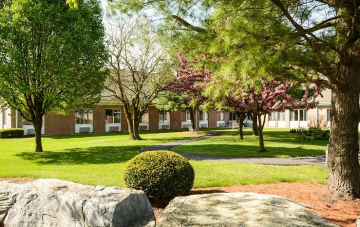 A tranquil garden scene with lush greenery and a brick building in the background.