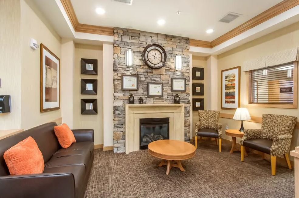 A cozy living room featuring a stone fireplace with a large clock, surrounded by comfortable seating and warm decor.