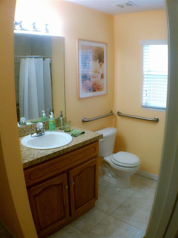 A small bathroom with a sink, toilet, and shower, featuring warm wall colors and decor.