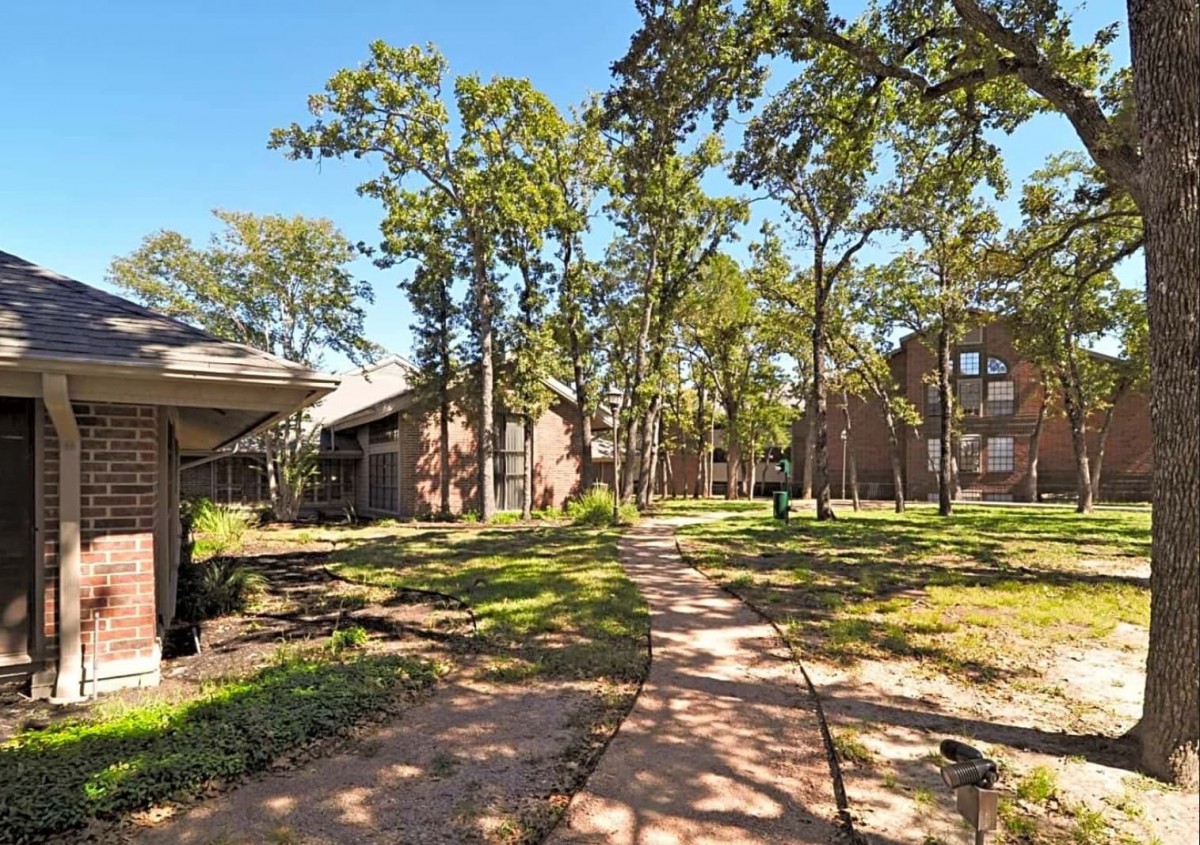 A sunny view of an apartment complex surrounded by trees and a winding pathway.