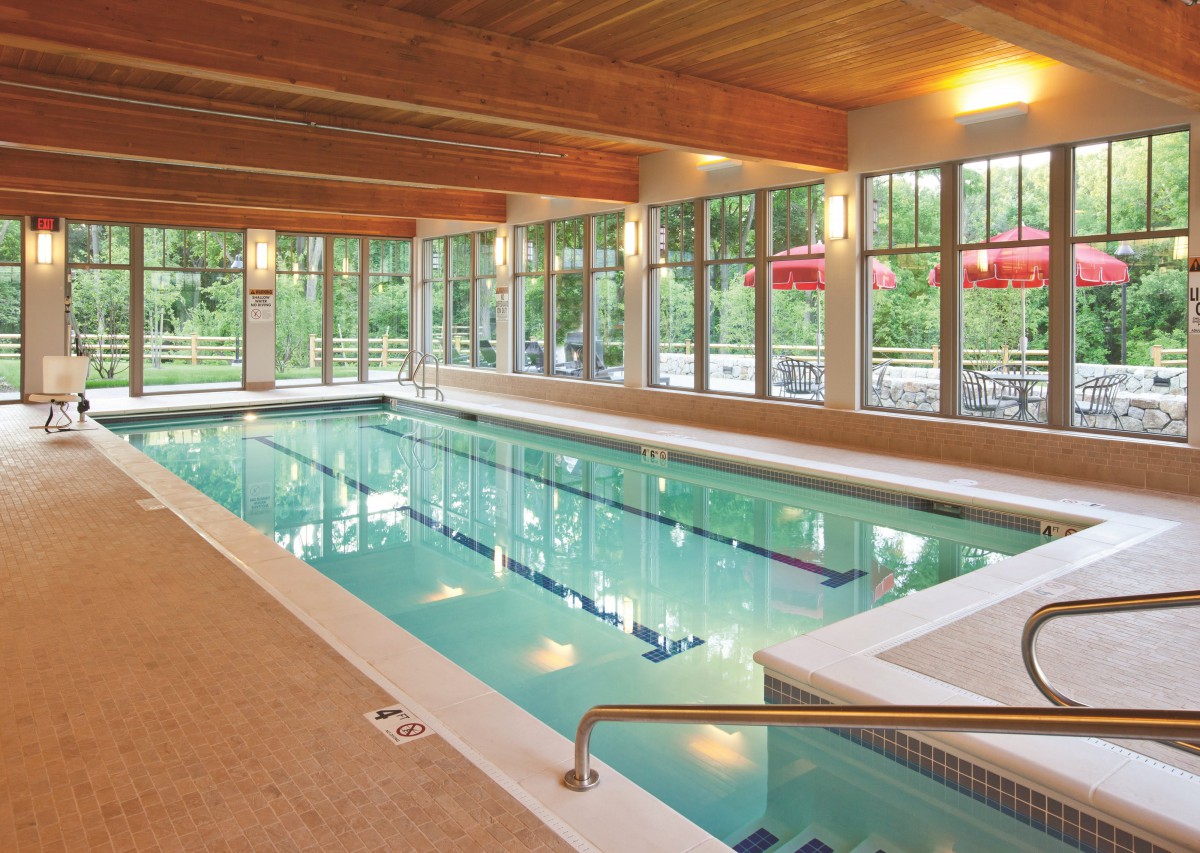 A serene indoor swimming pool with large windows and wooden ceiling beams.