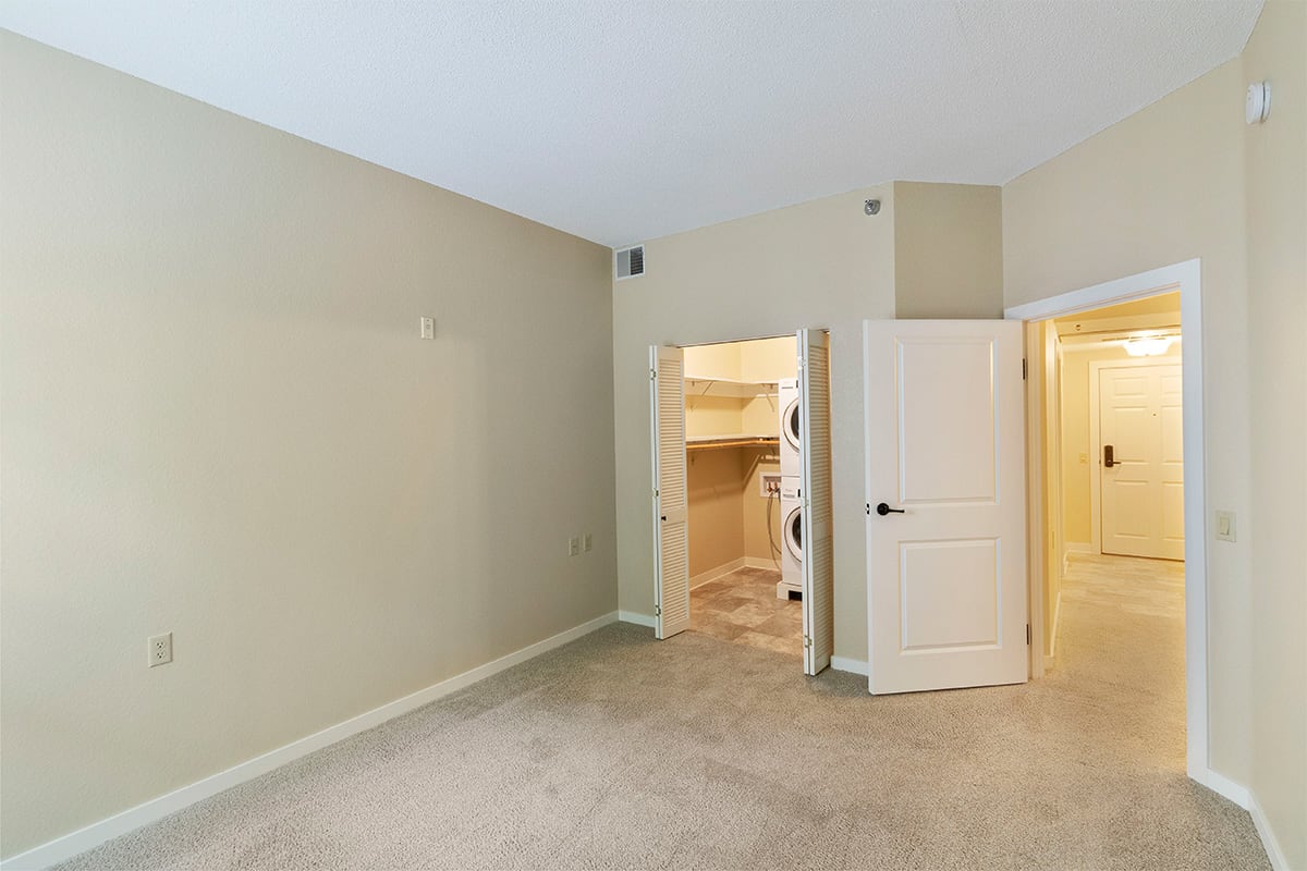 An empty room with beige walls and carpet, featuring an open doorway leading to another area.