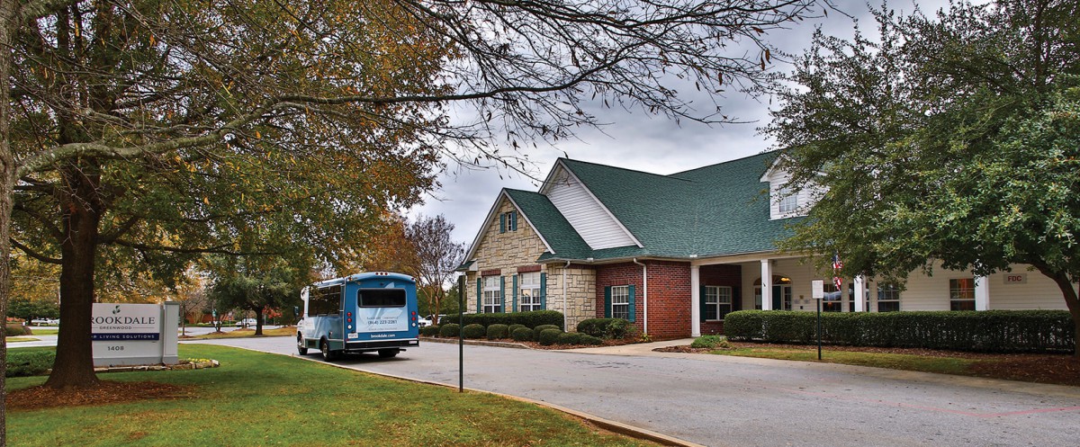 A blue bus parked in front of a suburban building on a cloudy day.
