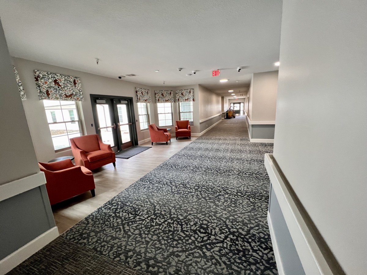 A bright hallway with red chairs and large windows, featuring elegant carpet and decor.