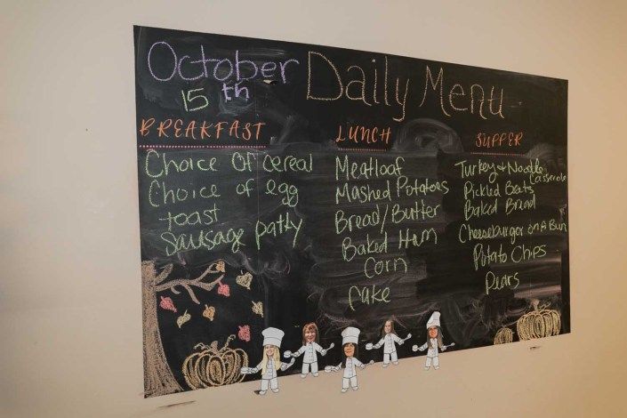 A chalkboard displaying the daily menu with breakfast, lunch, and dinner options for October 6th.