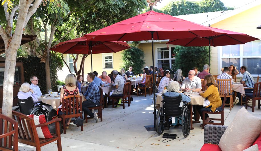 A group of people enjoying a meal together under red umbrellas at an outdoor restaurant.