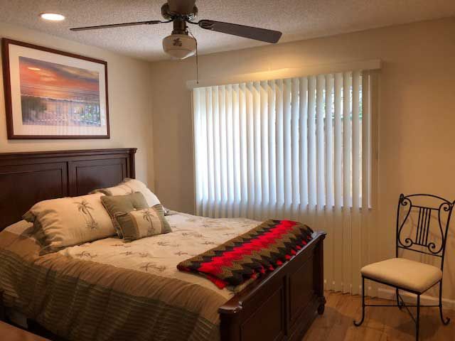 A cozy bedroom featuring a double bed with decorative pillows and a red-striped blanket, complemented by a ceiling fan and window blinds.