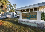 A van is parked near a building with a colorful sign, surrounded by trees.