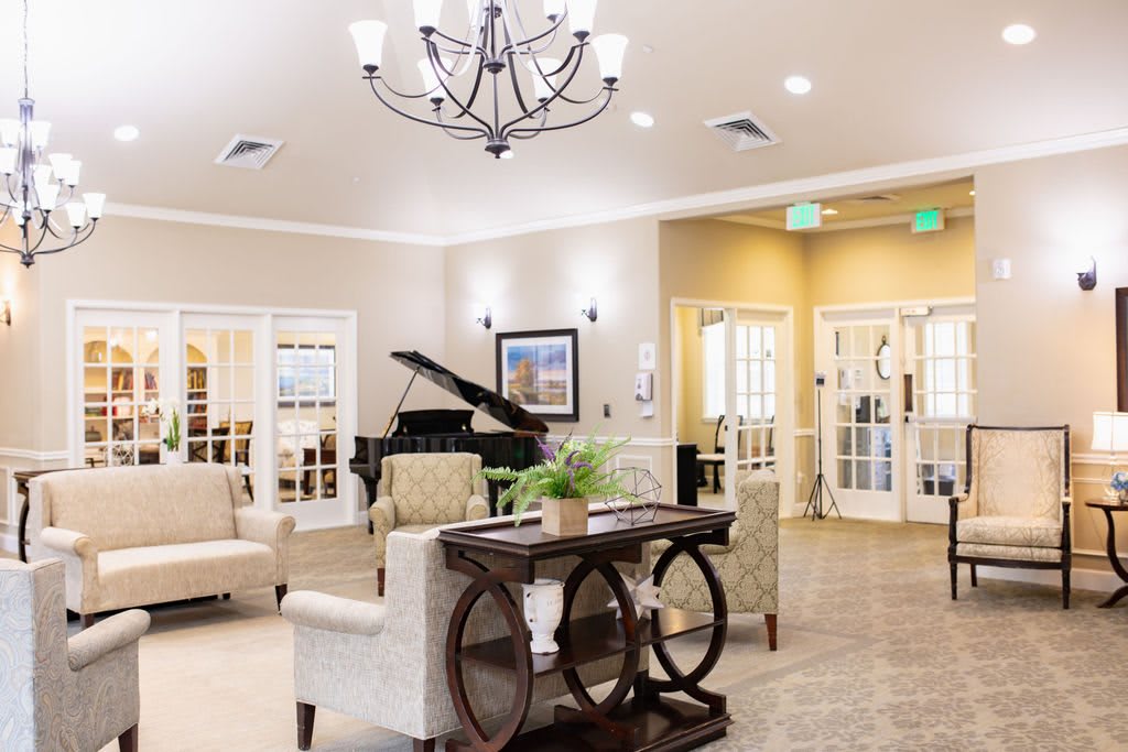 A spacious and elegantly decorated living room featuring a grand piano and chandelier.