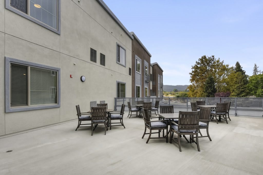 An outdoor patio area with several tables and chairs set against a building backdrop.