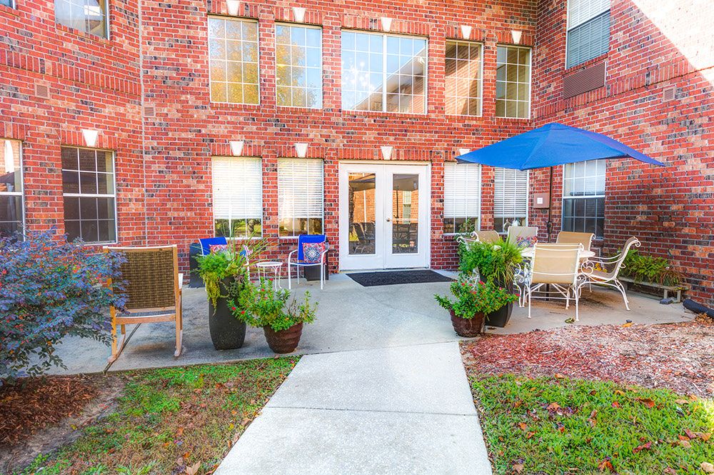 A brick building with an inviting outdoor seating area featuring a patio, plants, and umbrellas.