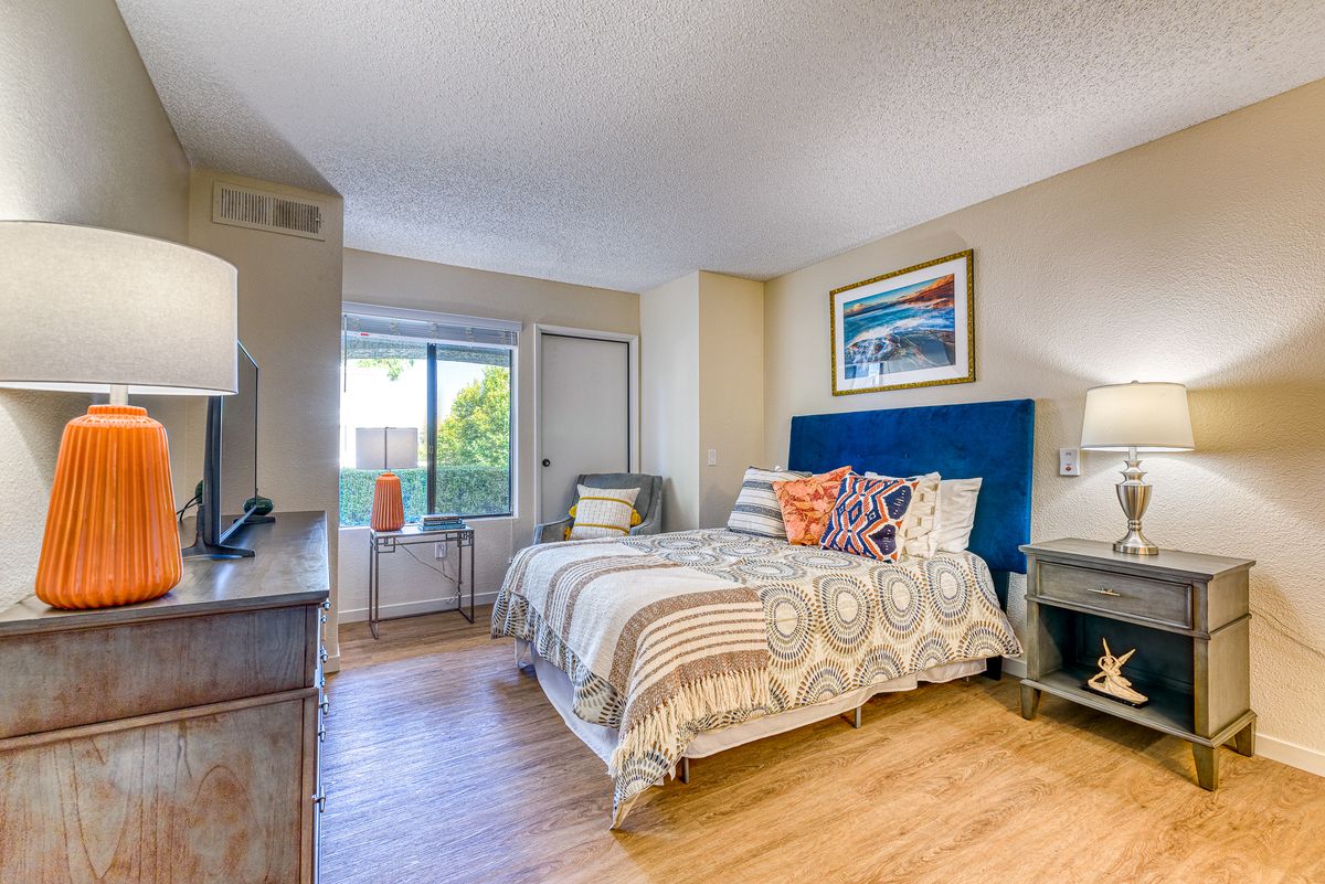 A cozy and modern bedroom with wooden flooring, featuring a stylish bed, colorful cushions, and abundant natural light.