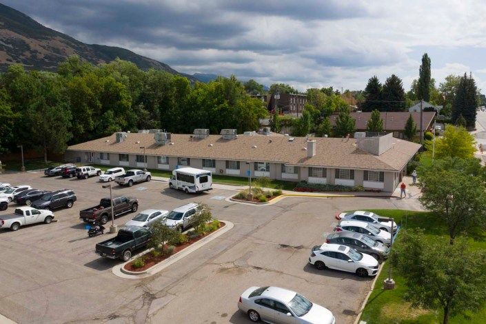 Aerial view of a parking lot with several cars and a building, surrounded by trees and mountains under a cloudy sky.