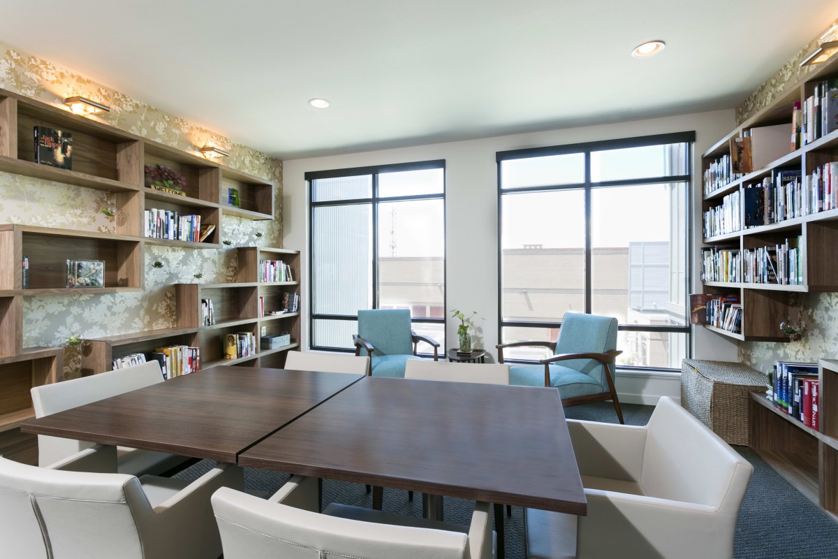A modern office meeting room with a large table, chairs, bookshelves, and natural light from the windows.