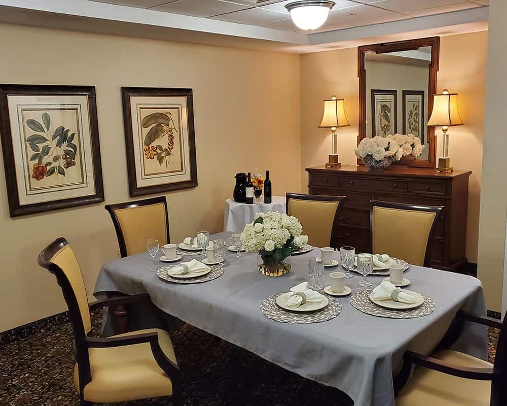 An elegantly set dining room with a table prepared for a formal meal, complete with chairs, artwork on the walls, and decorative lighting.