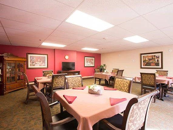A well-lit dining area with neatly arranged tables and chairs, adorned with decorative paintings.
