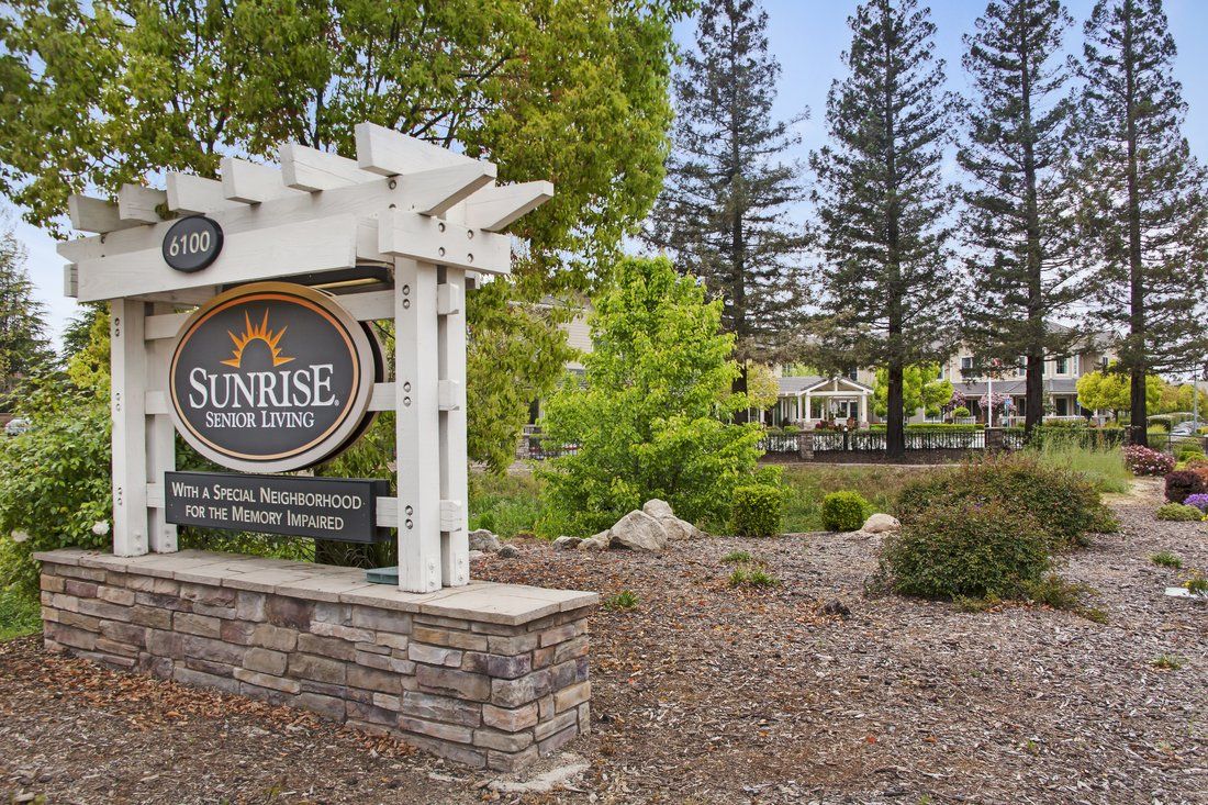 A landscaped entrance with a sign for Sunrise of Danville, featuring greenery and trees in the background.
