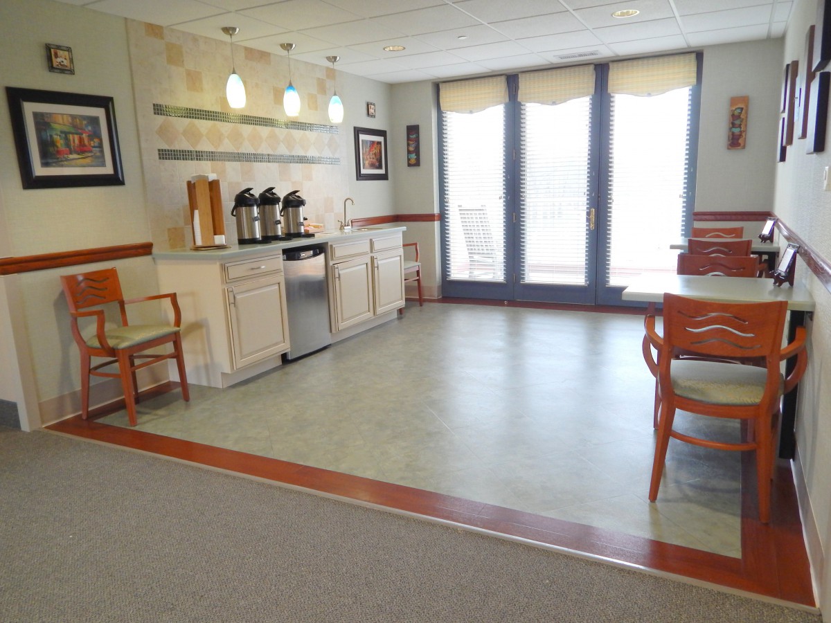 A cozy kitchen area with a coffee station, tables, and chairs by large windows.
