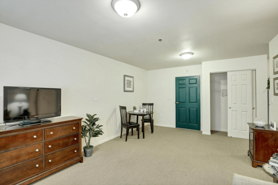 A minimalist living room featuring a small dining table, a television, and simple decor.