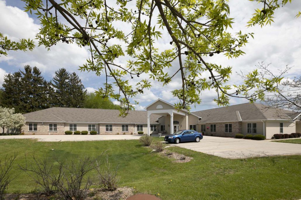 A healthcare facility with a parking lot and a car, surrounded by trees.