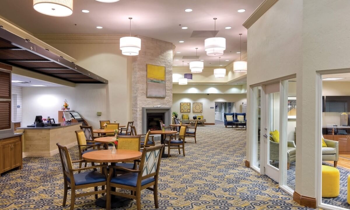A well-lit lobby area with tables and chairs arranged on a patterned carpet.