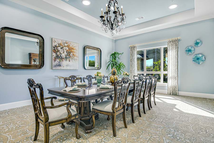 A beautifully decorated dining room featuring an elegant chandelier, a long dining table with chairs, and tasteful artwork on the walls.