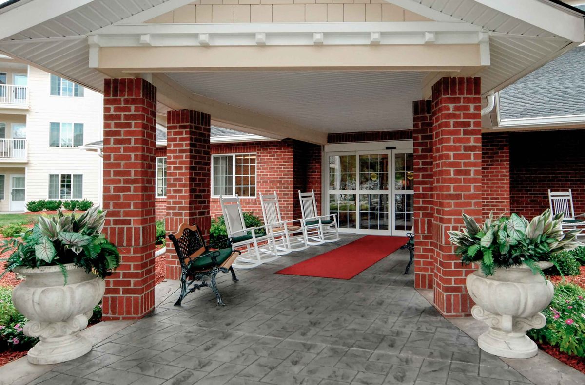 A welcoming entrance with red brick pillars, rocking chairs, and a red carpet leading to the doors.