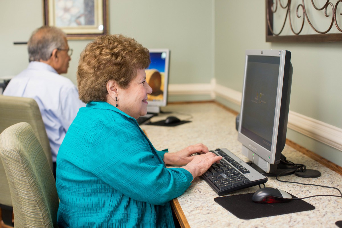 An elderly woman sitting at a desk using a computer, showcasing engagement with technology.