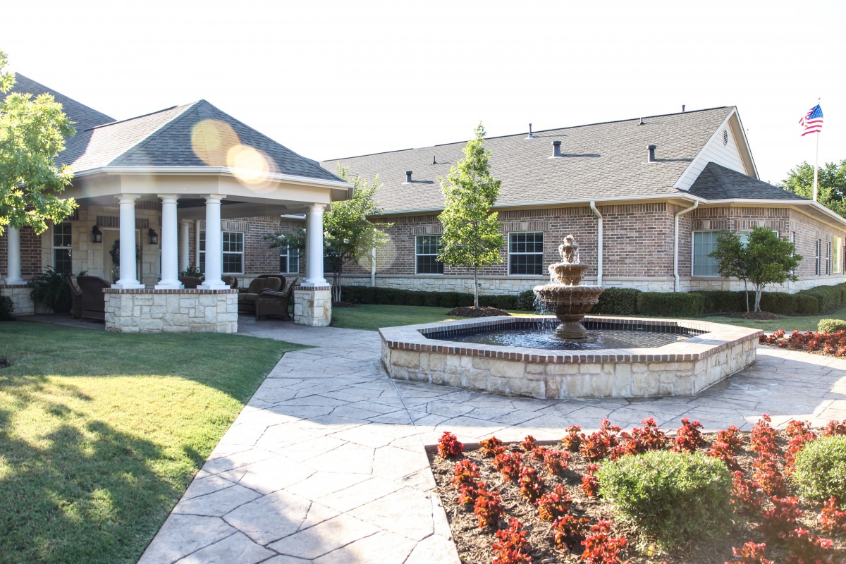 A beautifully landscaped courtyard featuring a fountain surrounded by flowers and a building in the background.
